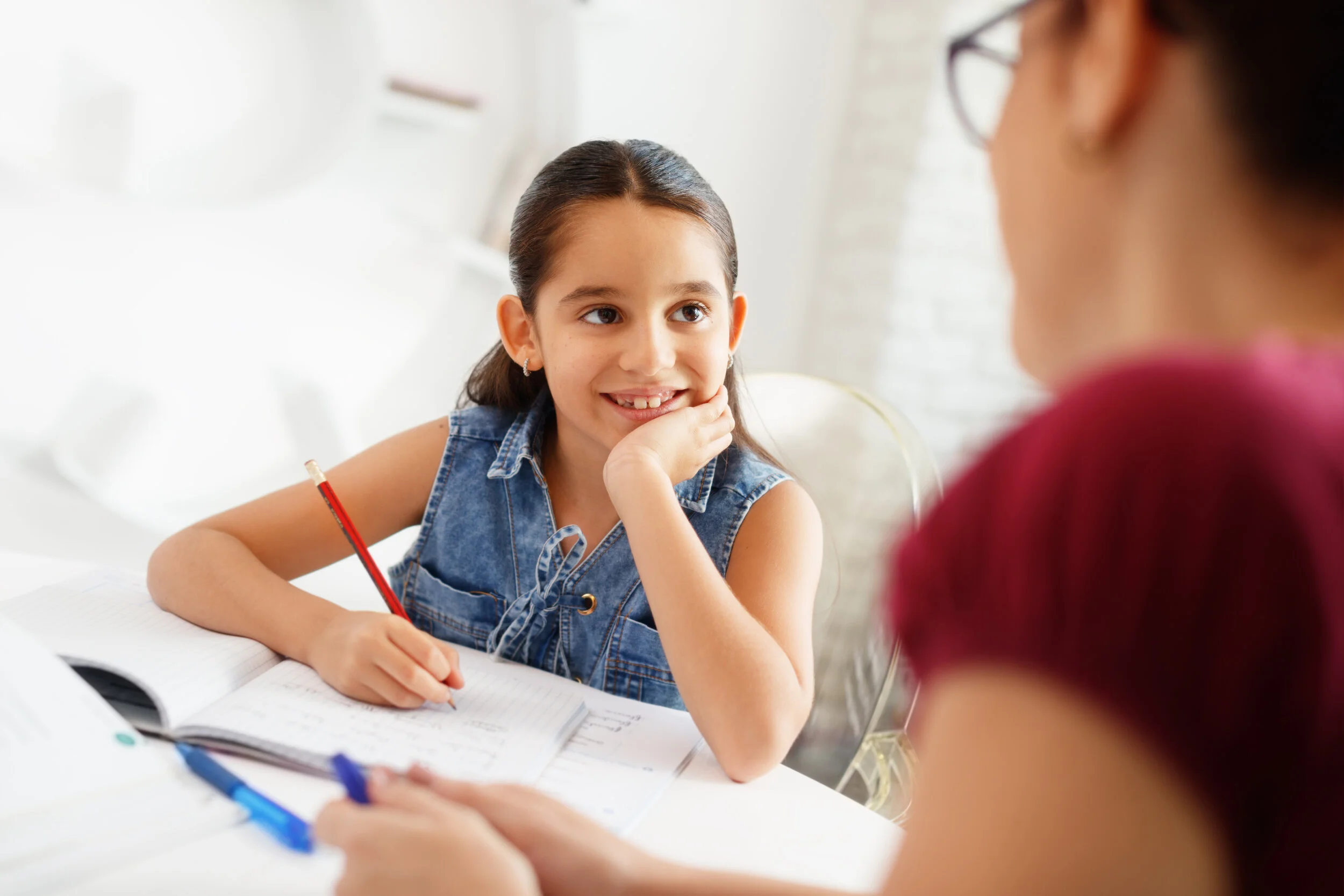 A tutor and a smiling girl working through a lesson together at a table.