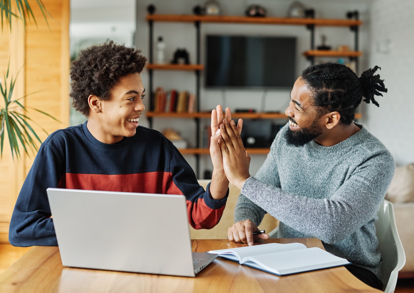 A volunteer tutor and a teenage student share a high-five over an open notebook.